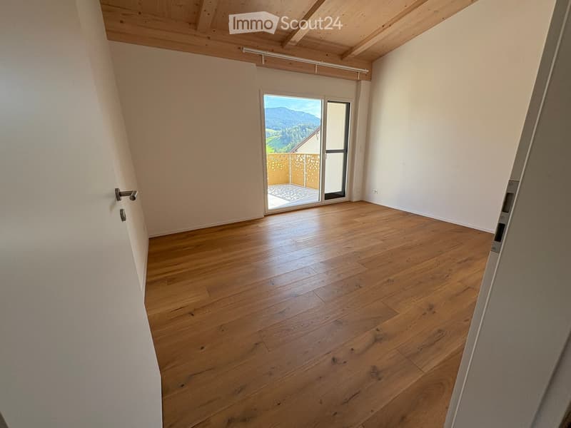 Empty room with wooden flooring, white walls, and a large sliding glass door leading to a balcony with a scenic mountain view.