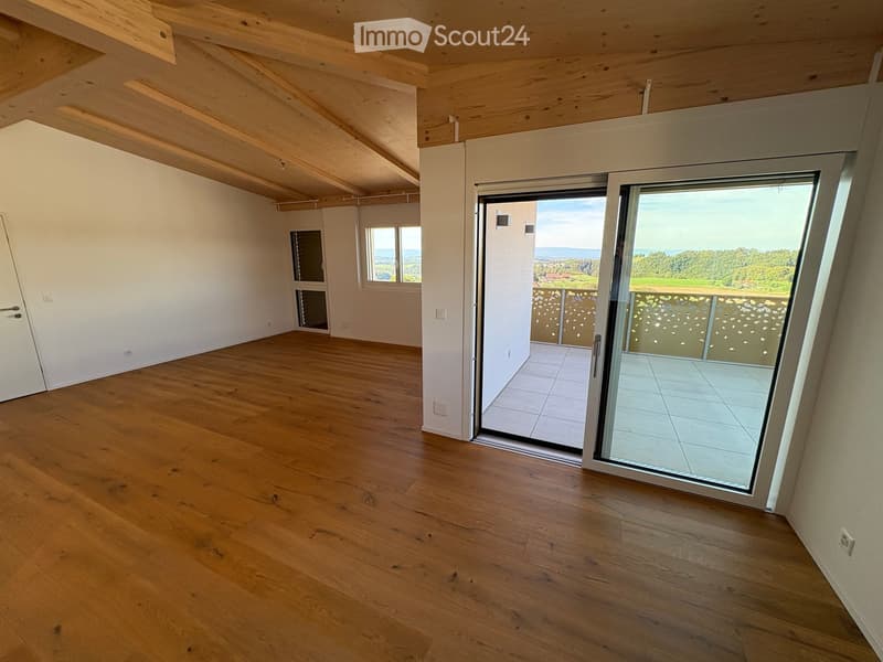Empty room with wooden flooring, white walls, large windows, and a sliding glass door leading to a balcony with a scenic view.