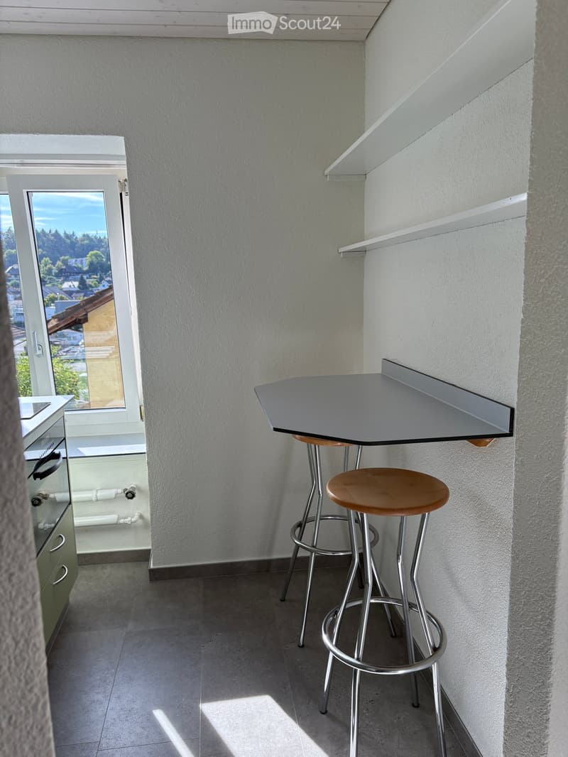 Balcony with a small table and two stools, overlooking a scenic view.