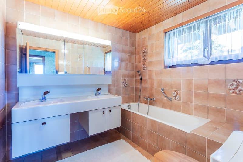 Modern bathroom with a double sink, large mirror, bathtub, and wooden ceiling.