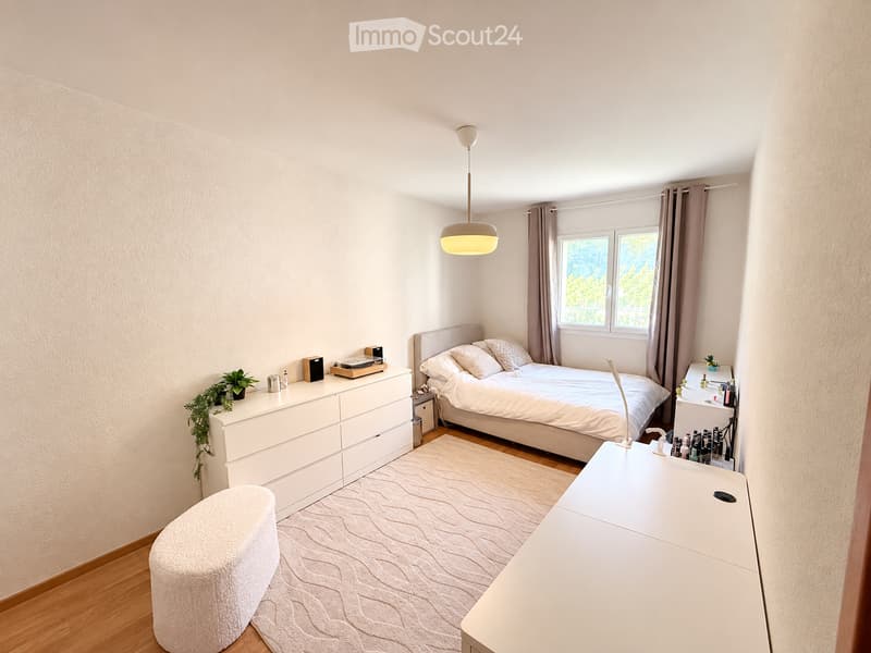 Modern bedroom with a large bed, nightstands, a round stool, a mirror, and a hanging lamp.