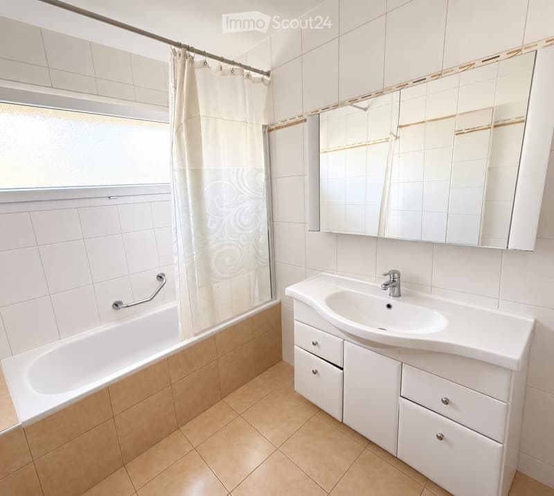 Modern bathroom with white tiles, a bathtub, a sink with a cabinet, and a large mirror above the sink.