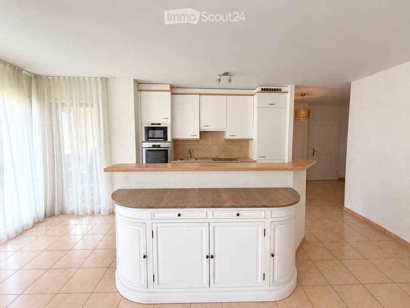 Modern kitchen with white cabinets, wooden countertops, built-in oven and microwave, sink with faucet, and a hanging light fixture.