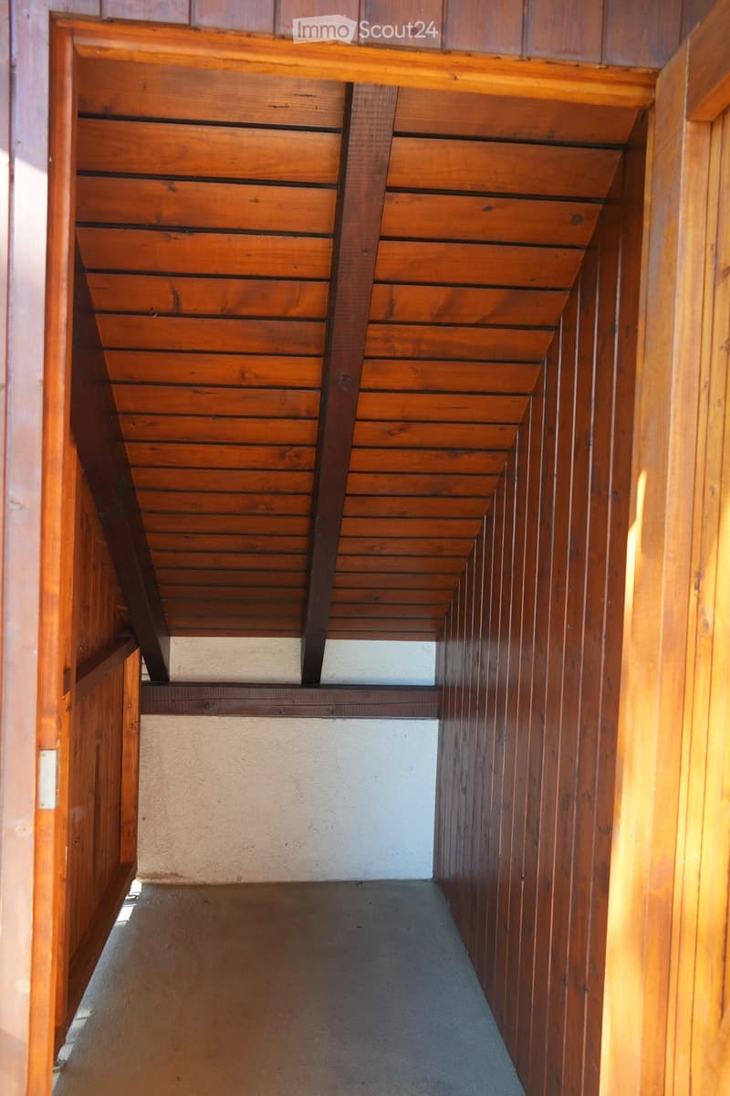 Wooden ceiling with slatted design and exposed beams, wooden walls, and a narrow hallway with a concrete floor.