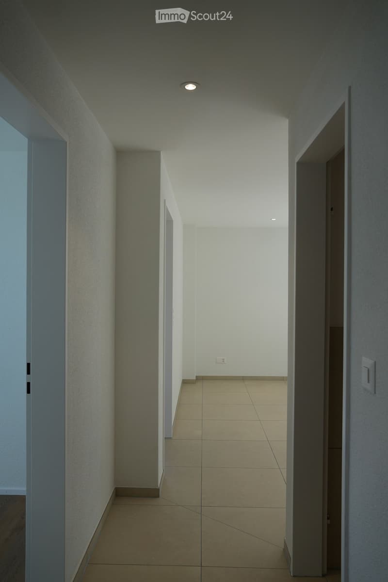 Modern hallway with beige tiled floor, white walls, recessed ceiling lights, and two open doorways on either side.