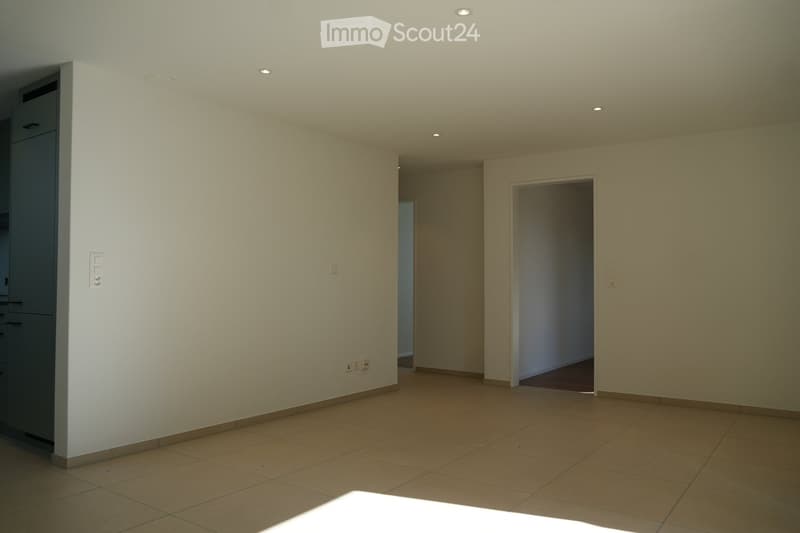 Empty room with tiled floor, white walls, and recessed ceiling lights. Two doors lead to adjacent spaces.