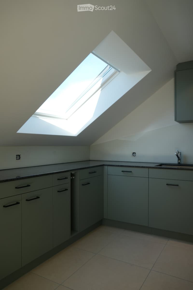 Modern kitchen with grey cabinets, tiled floor, and a large skylight window above the sink area.