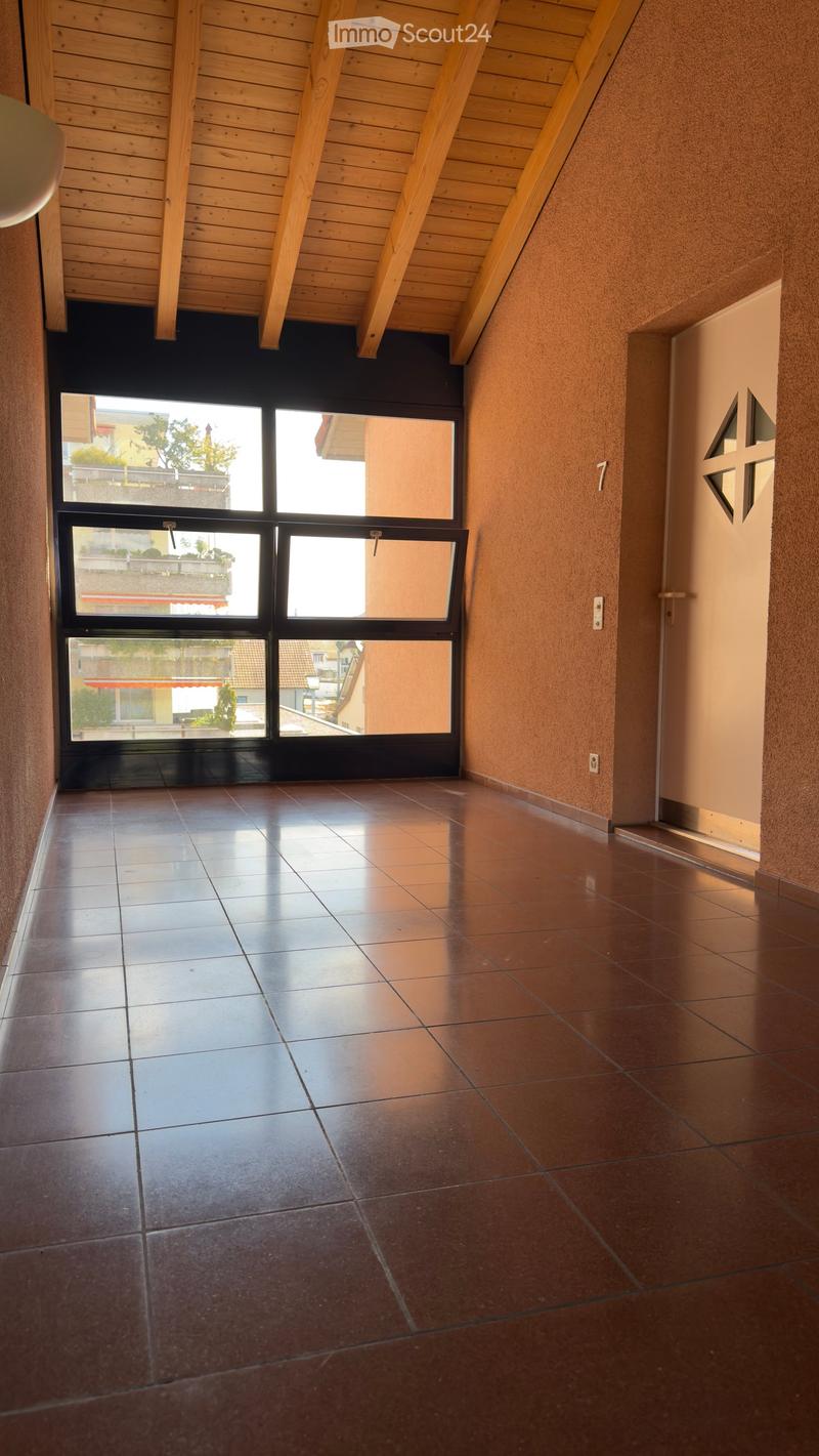 Empty hallway with tiled floor, wooden ceiling beams, and large windows showing outdoor view.