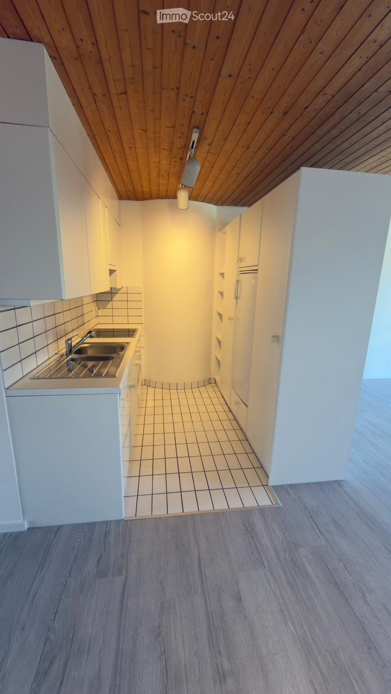Empty room with wooden ceiling, white cabinets, tiled floor, and a small sink area.