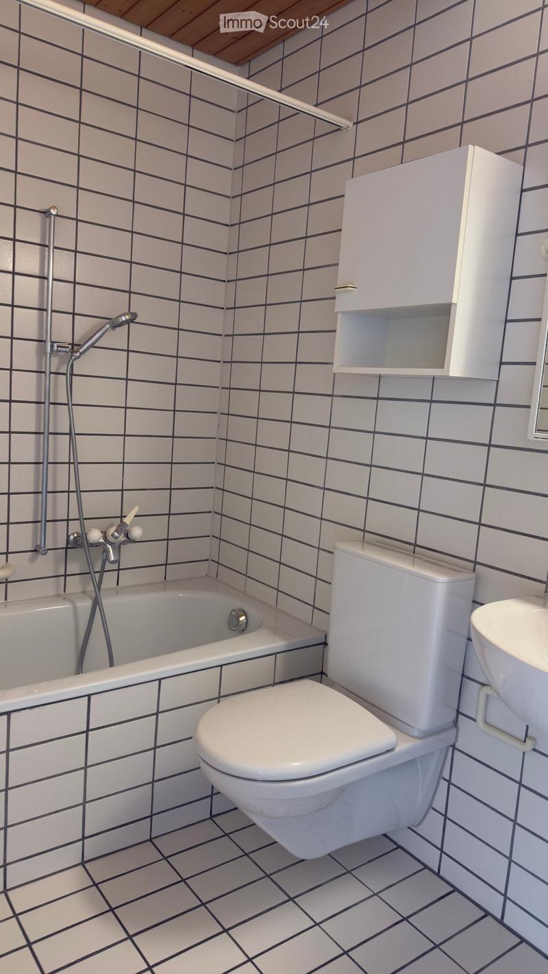 Modern bathroom with white tiles, black grid pattern, bathtub, toilet, sink, showerhead, and cabinet.