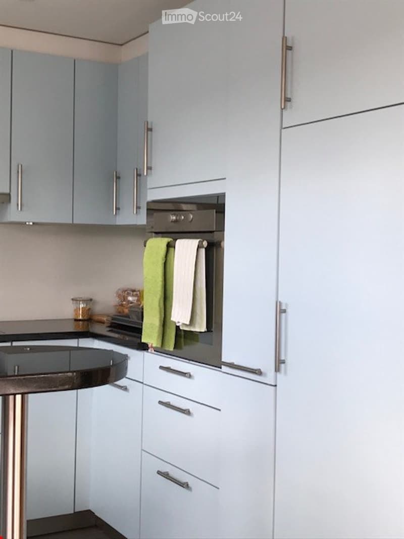 Modern kitchen with light blue cabinets, stainless steel appliances, a black countertop, and a small round table with a metallic base.