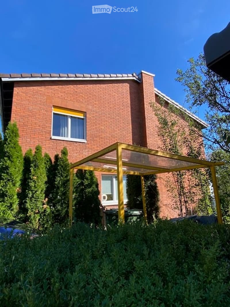 Two-story brick house with white-framed windows, surrounded by greenery and a small yellow patio structure.