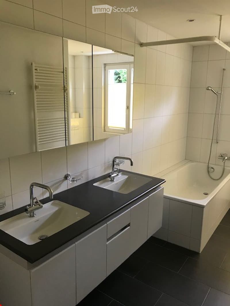 Modern bathroom with double sink vanity, bathtub, large mirror, and towel rack.