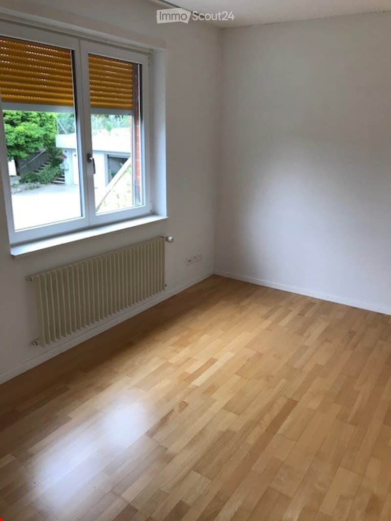 Empty room with wooden flooring, white walls, a radiator, and a window with blinds. No furniture or equipment present.
