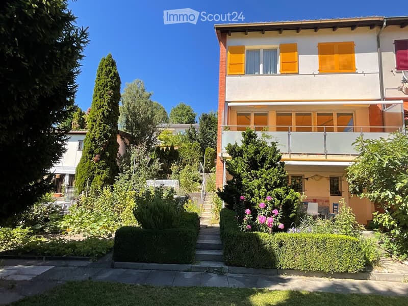 Two-story house with yellow shutters, balcony, garden, and steps leading to the entrance.