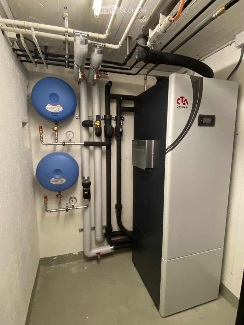 Utility room with water heater, pipes, valves, and gauges mounted on the wall.