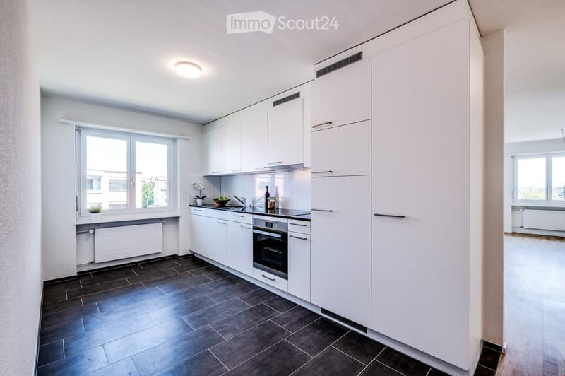 Modern kitchen with white cabinets, dark tiled floor, stainless steel oven, sink, and small decorative items on the counter.