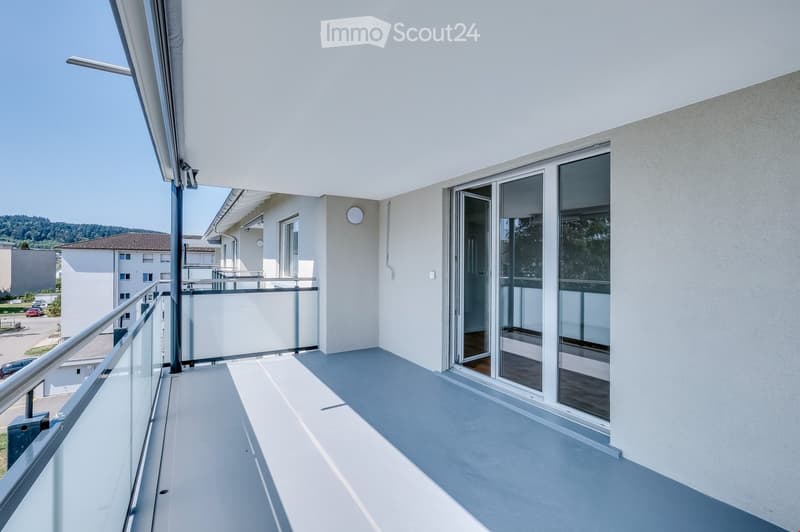 Modern balcony with glass balustrade, sliding glass doors, and a view of the surrounding area.