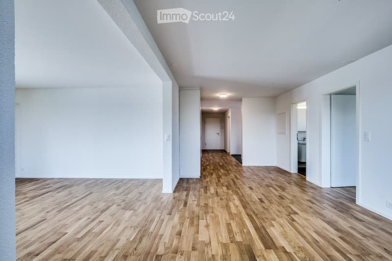 Bright, empty hallway with wooden flooring and white walls, leading to a partially visible bathroom area.