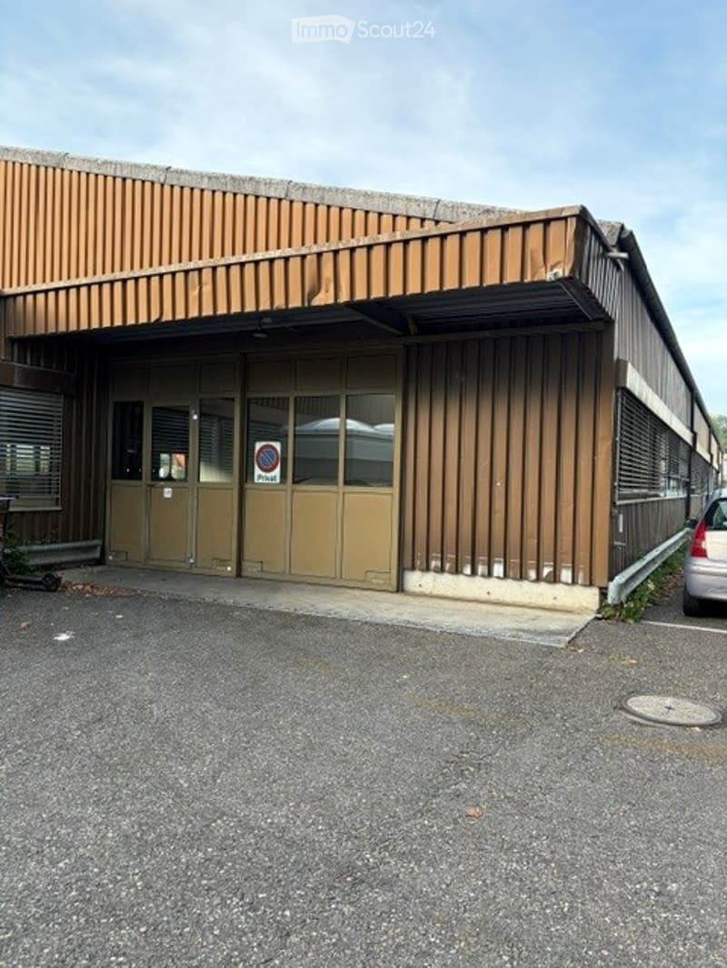 A single-story industrial or commercial building with a brown metal facade, large roll-up doors, and a small covered entrance area.