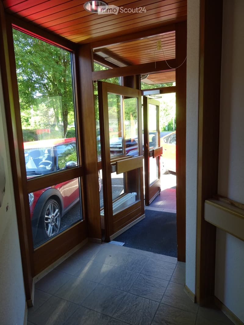 Entrance hallway with tiled floor, wooden doors, and large windows showing parked cars outside.