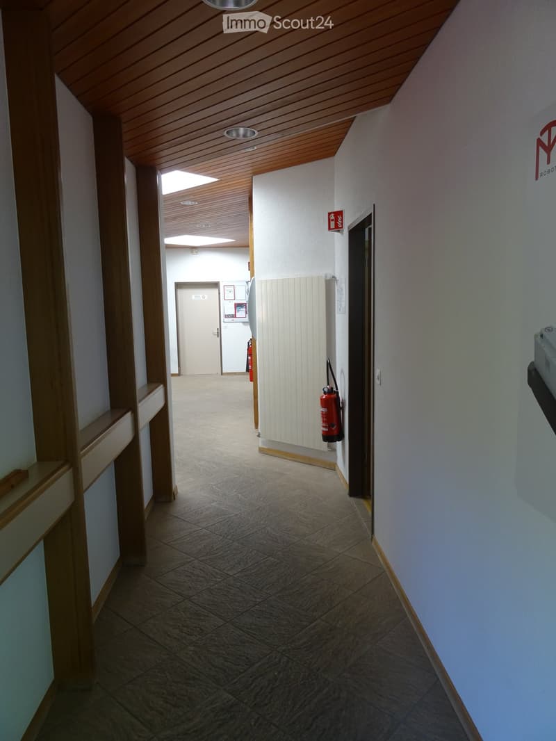 Clean hallway with tiled floor, wooden ceiling, and white walls. Features a fire extinguisher mounted on the wall and a partially open door leading to another area.