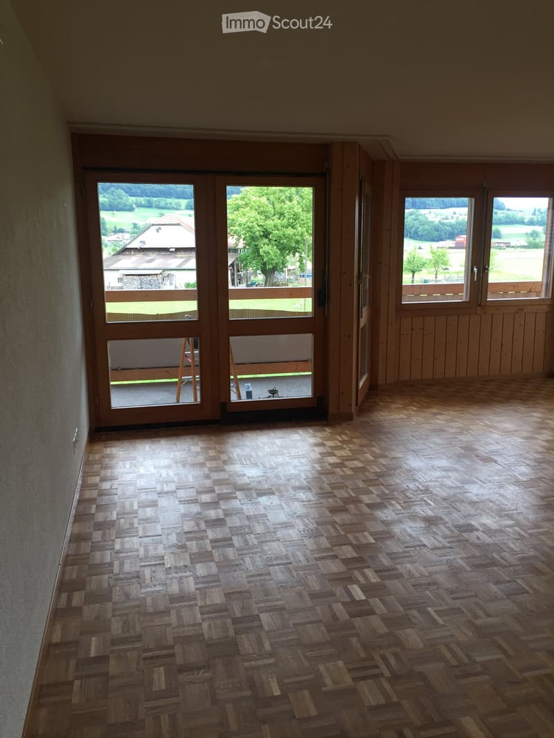 Empty room with wooden parquet flooring, large windows, and sliding glass doors leading to a balcony or outdoor area.
