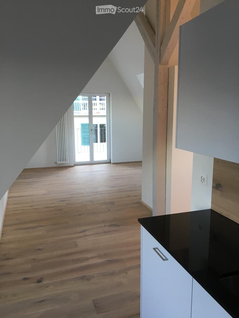 An unfurnished attic room with wooden flooring, white walls, and a sliding glass door leading to a balcony.