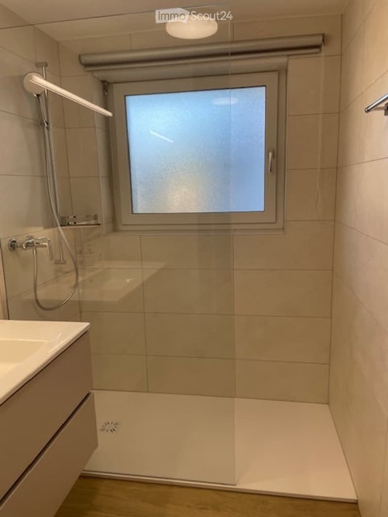 Modern bathroom with a large window, a walk-in shower with glass enclosure, a sink with a modern faucet, and a sleek showerhead.
