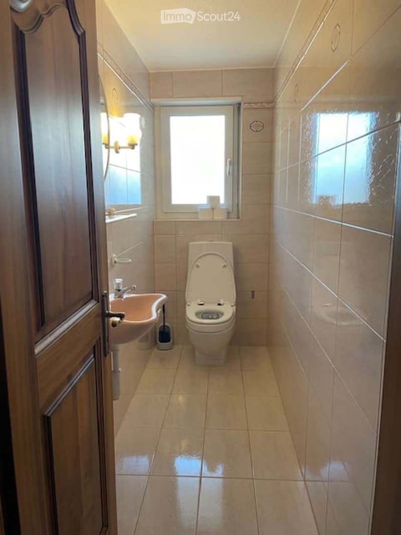 A small bathroom with beige tiles, a toilet, a sink, and a window letting in natural light.