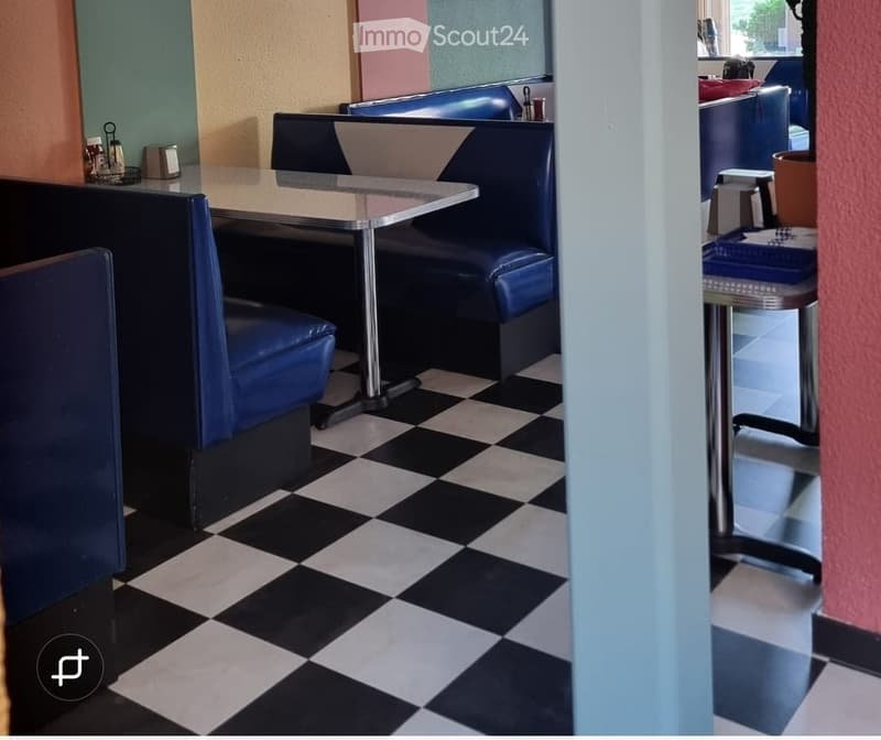 Retro diner interior with black and white checkered flooring, blue booth seating, and a small table with stools.