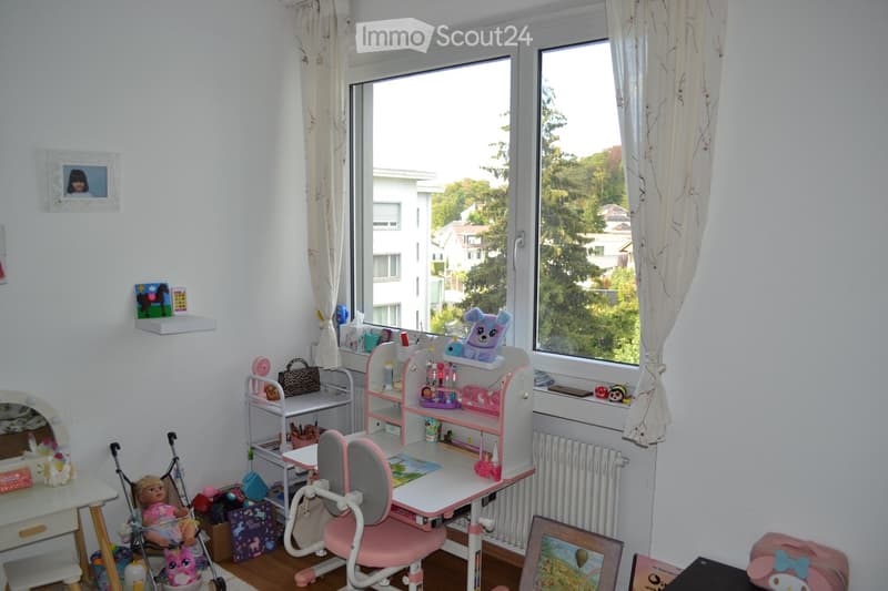 A well-lit children's room with a desk, chair, mirror, shelves, and various toys and decorations.