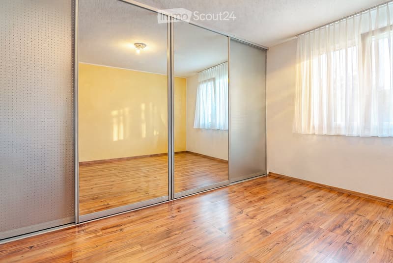 Empty room with wooden flooring, large mirrored sliding doors, and white curtains on windows.