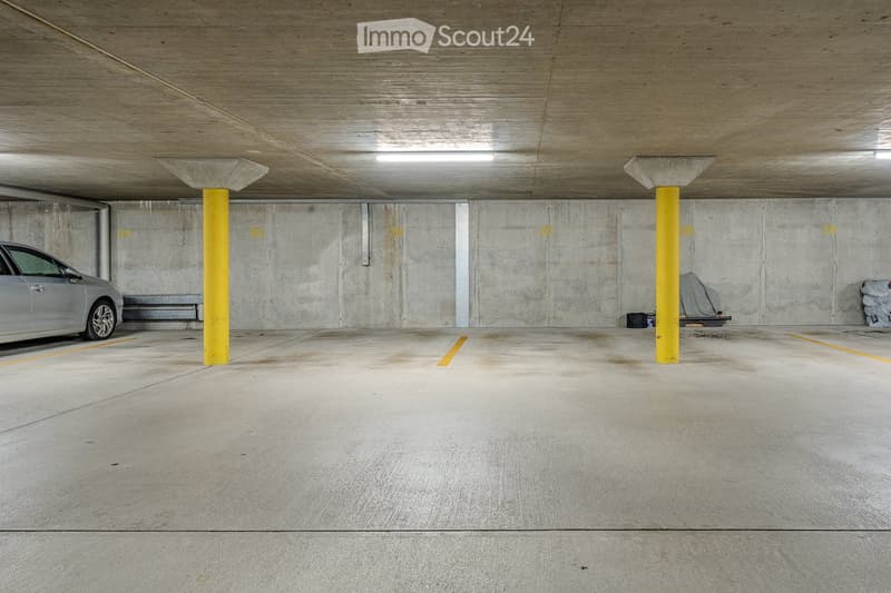 Underground parking area with concrete walls and floor, yellow pillars, and a parked car.