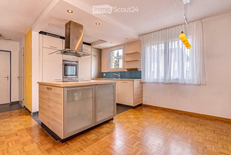 Modern kitchen with light wooden flooring, white cabinets, a central island, built-in oven, range hood, and pendant lights.