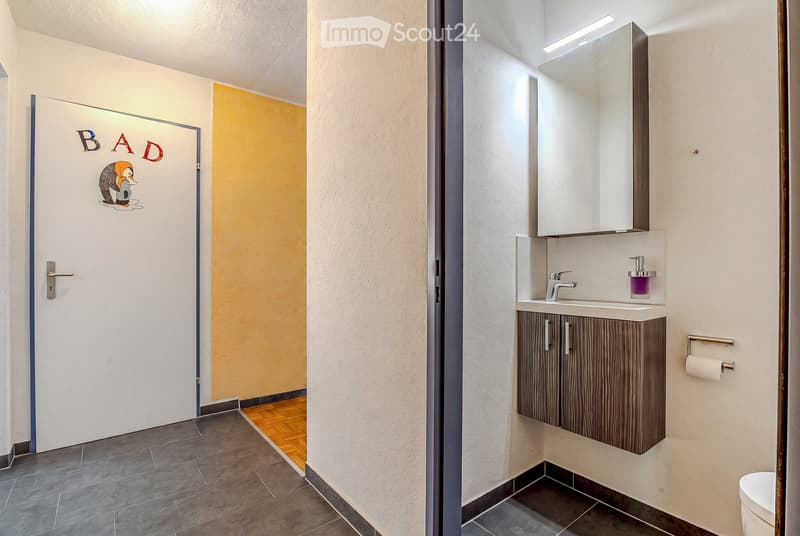 Modern bathroom with a sleek sink, mirror cabinet, and a door labeled "BAD" with a cartoon illustration.