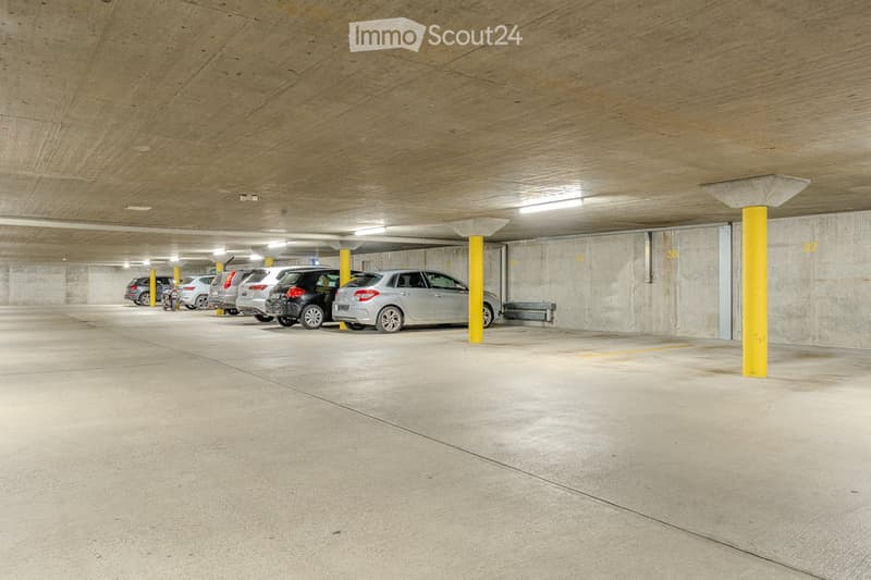 Underground parking area with several parked cars, concrete pillars, and numbered parking spots.