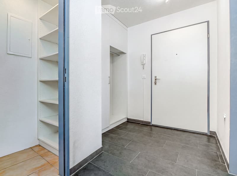 Empty room with white walls, grey tiled floor, built-in shelving unit, and a closed door.