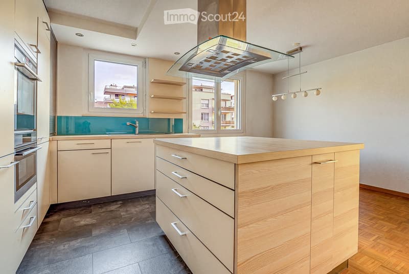 Modern kitchen with light wood cabinets, a central island, stainless steel appliances, and pendant lighting.