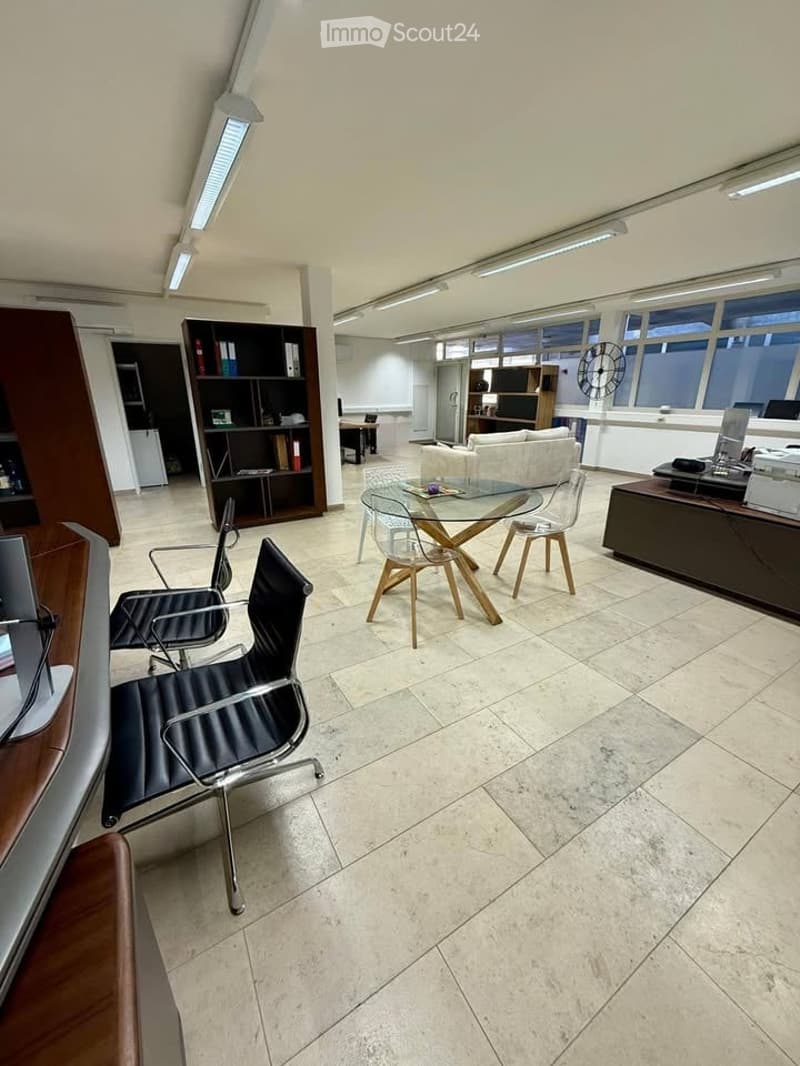 Modern office space with a glass table, chairs, a sofa, bookshelf, and office equipment.