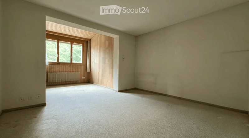 Empty room with beige walls, carpeted floor, and large windows with wooden frames. No furniture or equipment present.
