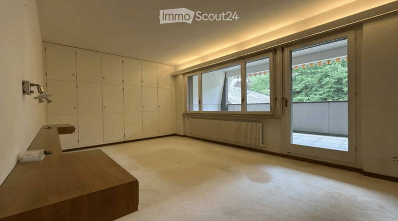 Empty room with large windows and a sliding door leading to a balcony, featuring built-in wardrobes and a small wooden bench.