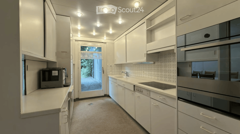 Modern kitchen with white cabinets, stainless steel appliances, and a large window overlooking a garden.