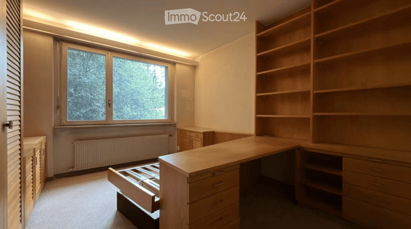 Empty room with built-in wooden shelving units, a desk, and a window with blinds. No furniture or personal items are present.