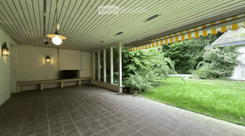 Covered outdoor space with tiled floor, wooden ceiling, and large windows overlooking a green garden.
