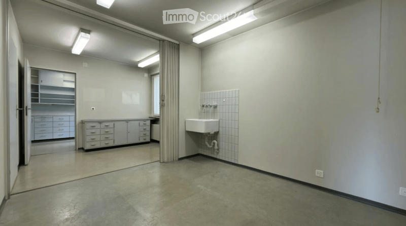 Empty bathroom with a sink, faucet, and cabinets. The walls are tiled, and the floor is concrete.