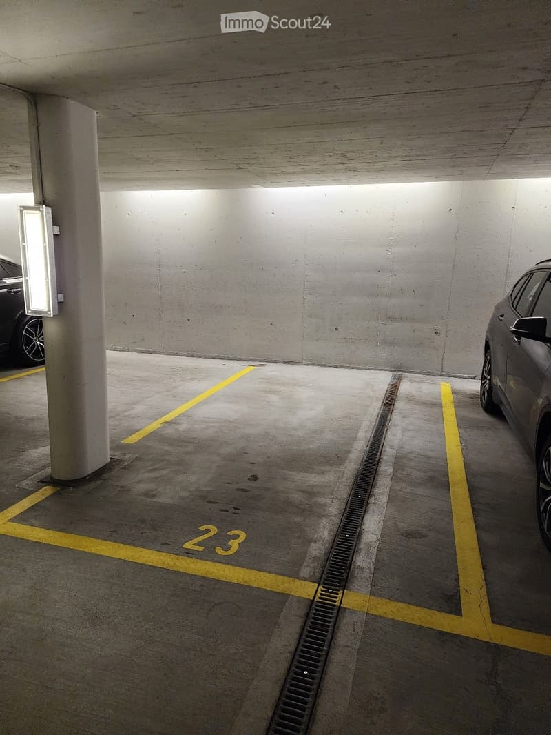 Underground parking area with marked parking spaces, concrete pillars, and two parked cars visible in the background.
