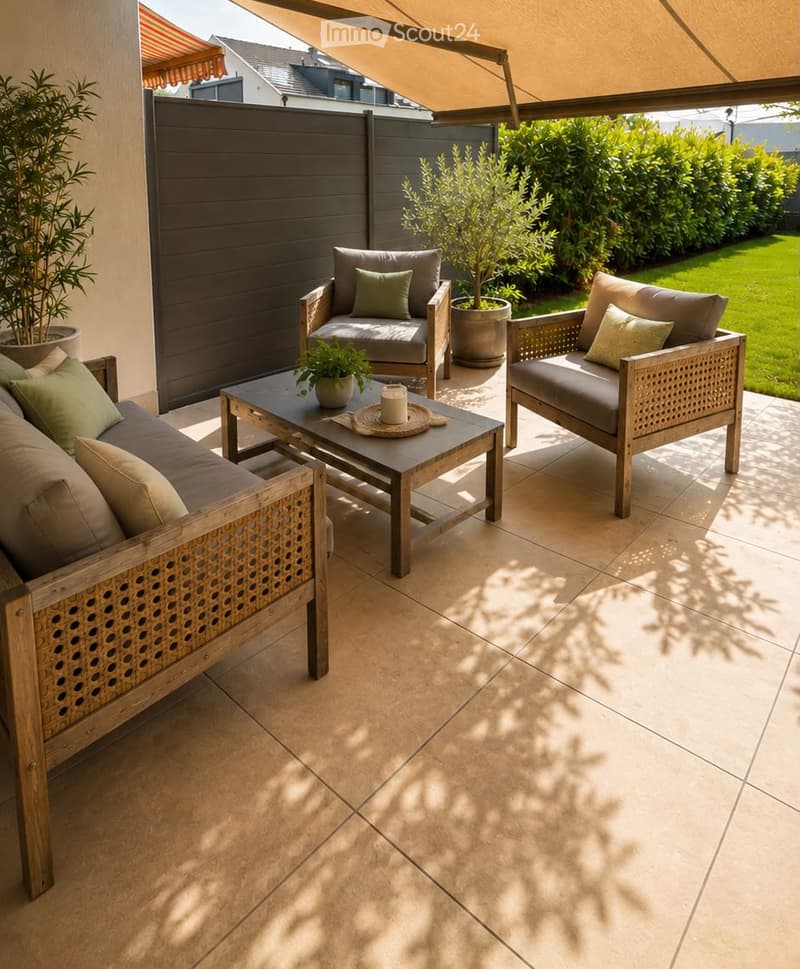 A modern outdoor patio with a tiled floor, featuring a sofa, two armchairs, a coffee table, and potted plants. The area is shaded by a large awning and enclosed by a wooden fence.