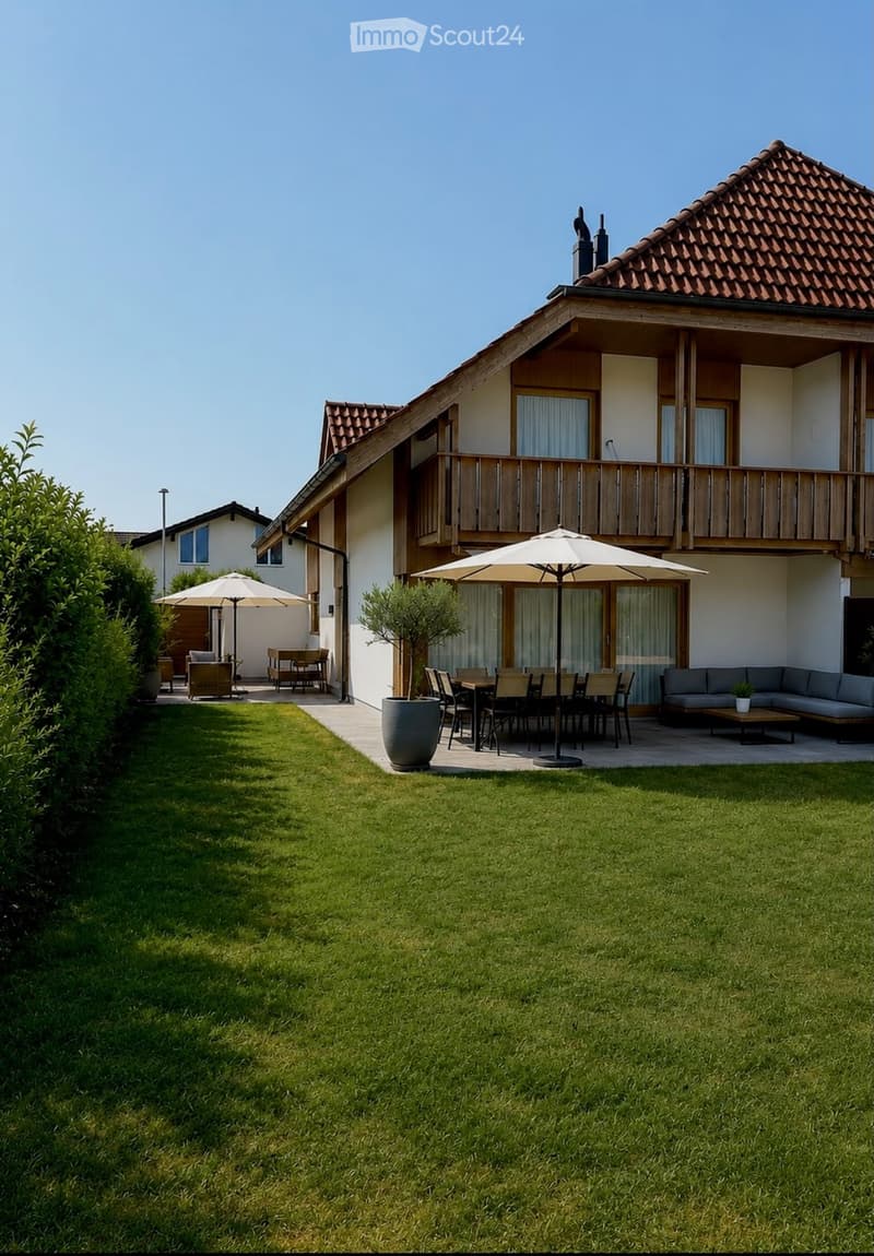 Lush green lawn with patio furniture, including a sofa, dining table, chairs, and umbrellas, near a modern house with a balcony and large windows.