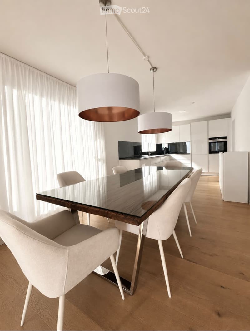 Modern dining area with a glass-top wooden dining table, white chairs, pendant lights, and a sleek kitchen in the background.